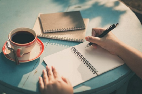 Writing in a notebook with a cup of coffee Image